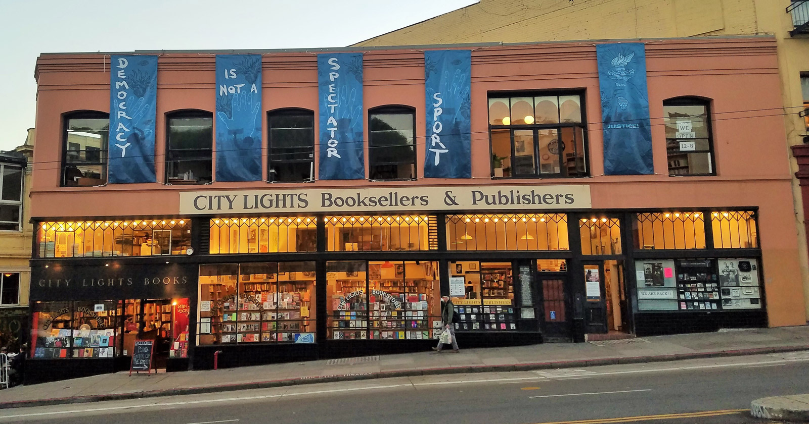 Lighted up City Lights storefront with banners that read DEMOCRACY IS NOT A SPECTATOR SPORT