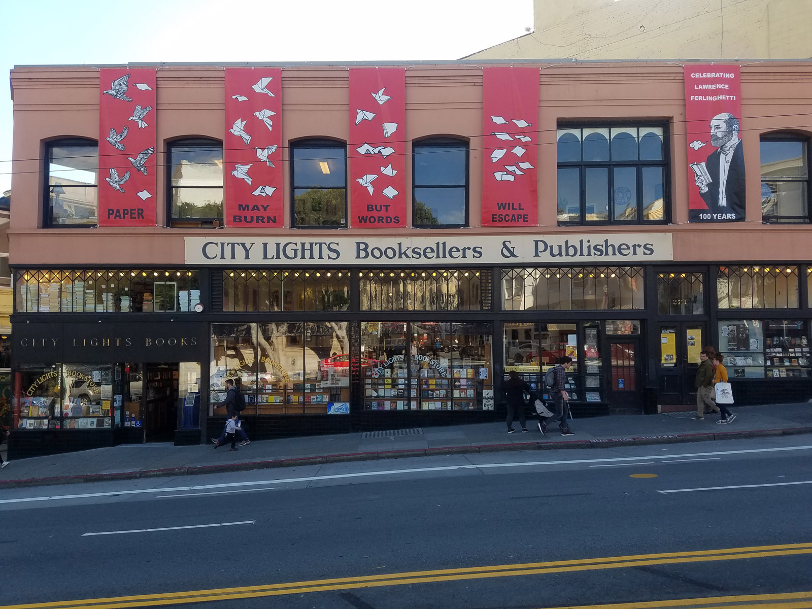 People walk by the City Lights storefront that is decorated with banners for Ferlinghetti's centennial