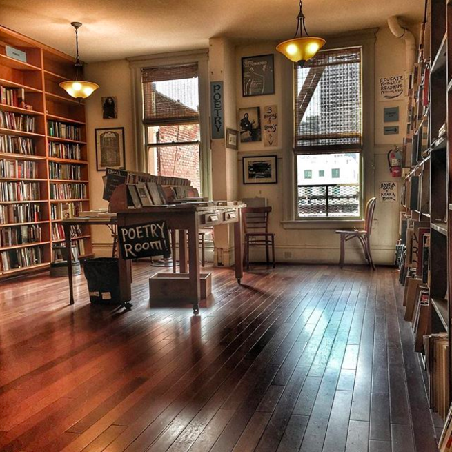 The upstairs poetry room, filled with bookshelves and a central table, in daytime 