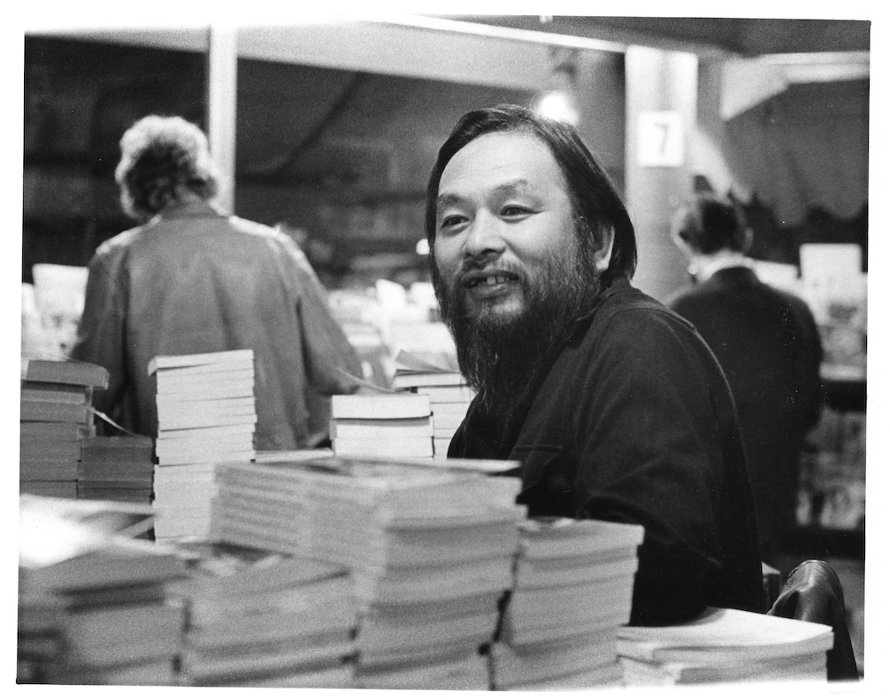 Portrait of a smiling Shigeyoshi Murao behind stacks of books 